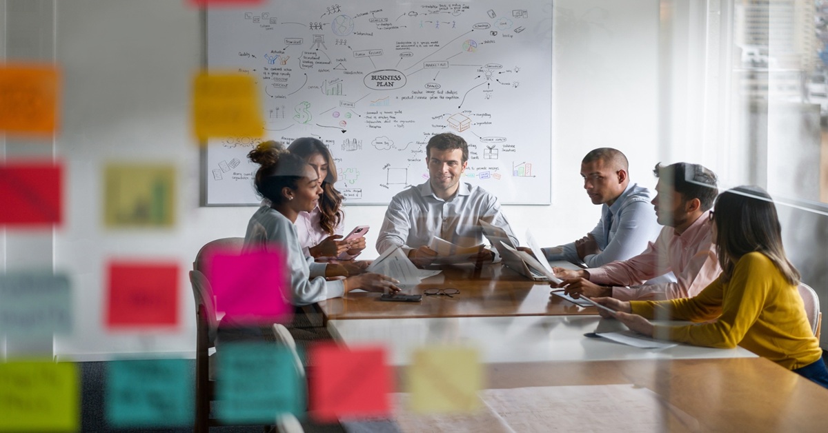 Professionals in a board room collaborating with post-its and a whiteboard